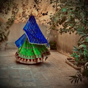 A woman in motion, wearing a vividly colored blue and green traditional dress that appears to swirl around her.